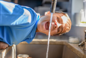 Foto eines Jungen, der Wasser direkt aus dem Hahn trinkt