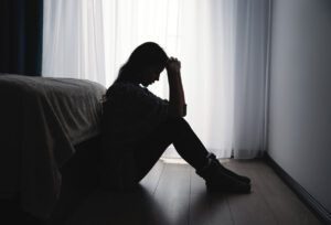 Symbolbild Depression: Mensch sitzt in dunklem Zimmer auf dem Boden