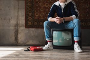 Auf einem Fernseher sitzender Jugendlicher