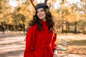 Bemützte Frau im roten Mantel vor herbstlicher Kulisse