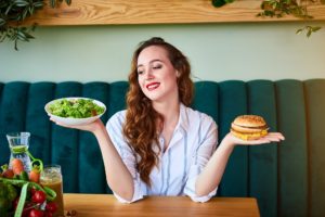 Junge Frau mit Salatschale und Burger in den Händen