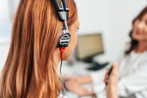 Audiologist doing impedance audiometry or diagnosis of hearing impairment. An beautiful redhead adult woman getting an auditory test at a hearing clinic.